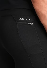 Leggings de sport Dri-FIT noirs avec une poche zippée, texture lisse et un design ajusté. Détails de couture le long des coutures.