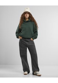 Grønn hettegenser med en frontlomme, kombinert med mørkegrå vide jeans. Antrekket fullføres med beige joggesko med grønne striper.