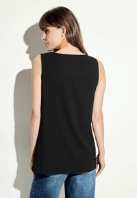 Top nero senza maniche in tessuto texturizzato con un design a schiena piatta. Presenta una linea dritta e un collo arrotondato, abbinato a jeans in denim blu.