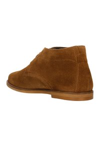 Stivaletti ankle in suede marrone con punta rotonda, semplici dettagli cuciti e un tacco in legno basso. Il design è elegante e minimalista.