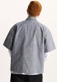Short-sleeve shirt in blue and white vertical stripes, featuring a relaxed fit, wide collar, and a smooth textured fabric.