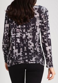 Långärmad topp i svart och grå abstrakt mönster, tillverkad av mjukt material med rund halsringning och avslappnad passform. Har en något rundad nederkant.