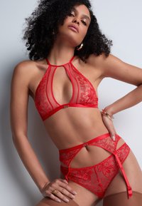 Ensemble de lingerie en dentelle rouge comprenant un soutien-gorge à col halter avec des panneaux transparents, une broderie florale, et des bretelles rythmiques sur le slip assorti avec des détails.