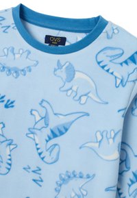 Camisa de manga larga de forro polar azul claro con ribete azul, que presenta un estampado de dinosaurios en diferentes tonalidades de azul y blanco. Etiqueta visible en el escote.