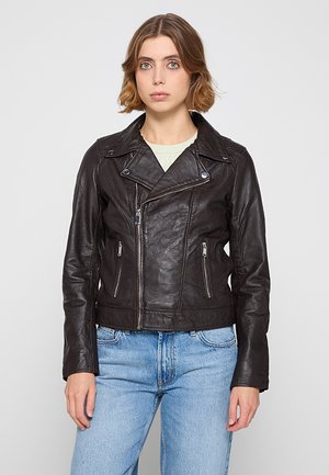 Veste de moto en cuir noir avec une coupe courte, des poches zippées et de larges revers, portée sur un haut vert clair et un jean bleu.