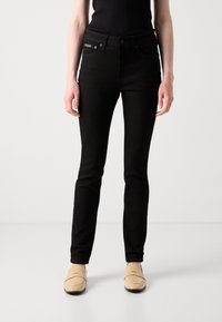 Zwarte skinny jeans met een klassiek ontwerp. Voorzien van steekzakken, een ritsopening en een gestructureerde stof. Gekleed met beige instapschoenen.