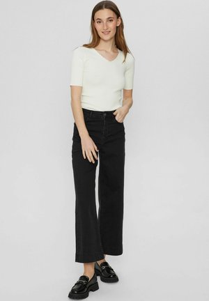 Haut blanc à manches courtes avec un col en V festonné, associé à un jean en denim noir à jambes larges et des mocassins noirs à semelle épaisse.