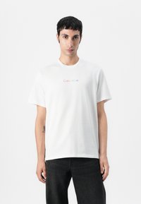 Witte katoenen t-shirt met een ronde hals en korte mouwen. De voorkant toont een meerkleurig "Calvin Klein" logo in een minimalistisch ontwerp.