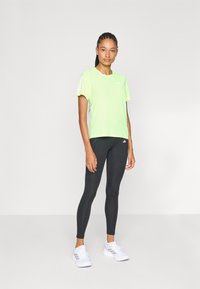 Lichtgroene sportt-shirt met korte mouwen en reflecterende accenten, gecombineerd met zwarte leggings en witte sneakers. Soepele stof en aansluitend ontwerp.