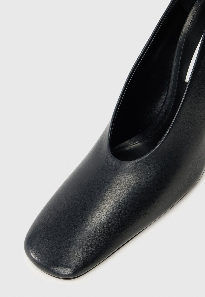 Schwarzer Leder-Hochschuh mit abgerundetem quadratischem Zehenbereich, glatter Textur und offenem Seitendesign, das eine minimalistische Ästhetik präsentiert.