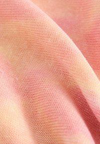 Gros plan sur un tissu tricoté doux dans des tons roses et pêche, montrant une texture fine et de doux plis.