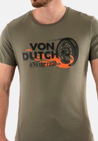 Camiseta verde oliva de algodón con un estampado de una llanta y llamas en negro y naranja, con el texto "VON DUTCH" y "On the road".