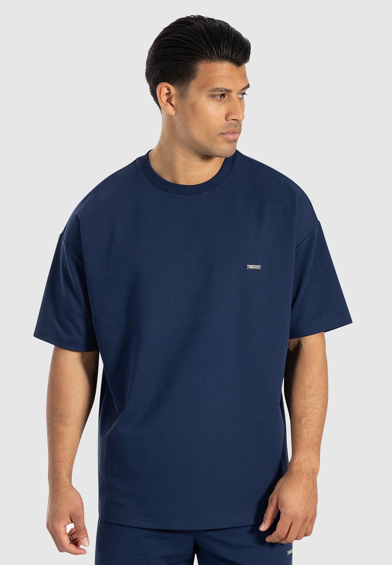 T-shirt in cotone blu navy con maniche corte, collo rotondo e un piccolo logo sul petto. Tessuto liscio e vestibilità rilassata.