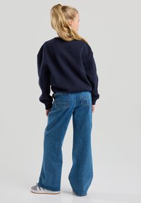 Navy blue sweatshirt, loose fit, paired with high-waisted, wide-leg light blue jeans featuring back pockets. Fabric appears soft and textured.