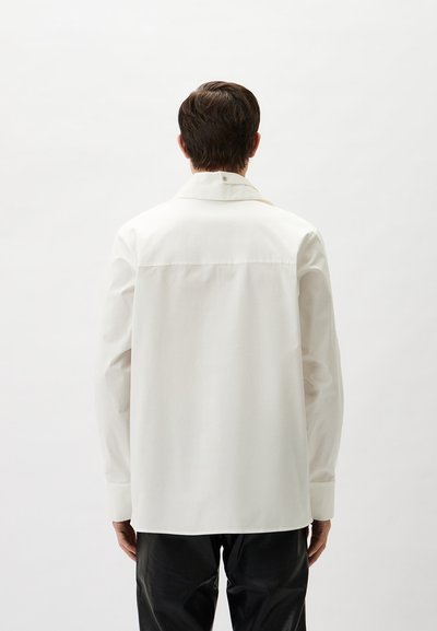 White oversized shirt with a classic collar, long sleeves, and button detail on the back. Smooth texture and relaxed fit.