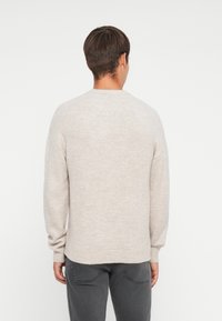 Beige strikket sweater med lange ærmer og ribbede manchetter. Rund halsudskæring og afslappet pasform, båret med grå bukser. Glat tekstur og letvægts.