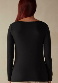 Schwarzes Langarmoberteil mit Bootsausschnitt, aus glattem Stoff, mit tailliertem Design, minimalen Nähten und einem leicht geschwungenen Saum.