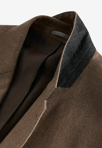 Brown wool blend jacket with a black felt collar. Interior features a patterned lining, showcasing a diagonal diamond texture.