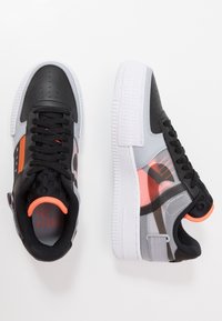 Svarta och grå sneakers med en texturerad yta, vit sula, orange detaljer och svarta skosnören med ett perforerat mönster.