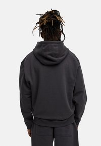 Dunkelgrauer Kapuzenpullover mit lockerer Passform, ausgestattet mit gerippten Bündchen und Saum. Glatte Textur, minimalistisches Design, keine sichtbaren Logos.