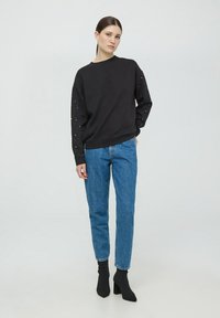 Czarna bluza z ozdobnymi rękawami, zestawiona z dopasowanymi niebieskimi dżinsami. Stylizacja uzupełniona jest ciemnymi botkami za kostkę oraz prostym wzorem.