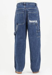 Pantaloni cargo in denim blu scuro con vestibilità ampia, dotati di molteplici tasche, una grande grafica bianca sul retro e dettagli con cuciture chiare.