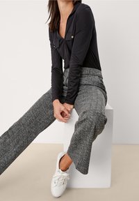 Body a maniche lunghe nera con due tasche frontali, abbinato a pantaloni grigi a coste con motivo a spina di pesce e sneakers bianche.
