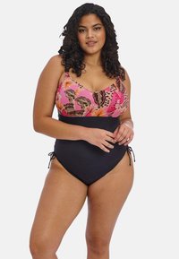 Plavky se vzorem růžových květin nahoře a černým spodkem. Vyrobeno z hladkého materiálu, s nastavitelnými bočními vazy a přiléhavým střihem.