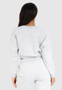 Felpa grigia corta con maniche lunghe e colletto rotondo. Texture morbida, vestibilità rilassata e polsini a coste. Indossata con pantaloni jogger grigi abbinati.