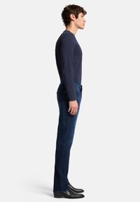 Camicia a maniche lunghe color blu navy abbinata a jeans blu scuro, caratterizzata da una vestibilità slim e una trama liscia, completata da stivali in pelle nera.