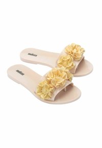 Chanclas de gel rosa con un acento floral de pétalos de goma amarillos a lo largo de la tira y una suela plana. Nombre de la marca "melissa" impreso en la plantilla.