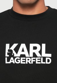 T-shirt in cotone nero con grafica bianca del nome "KARL LAGERFELD" e logo silhouette. Girocollo e texture a coste.