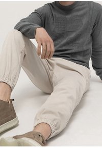 Gray textured sweater with a crew neck, paired with light beige jogger pants, featuring elastic cuffs and taupe sneakers with white soles.