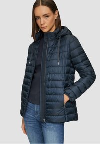 Veste réversible bleu marine avec un design matelassé horizontal, fermeture éclair, capuche ajustable et poches latérales. Matériau doux et léger.
