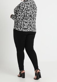 Czarno-biała bluzka w panterkę z długim rękawem, zestawiona z czarnymi obcisłymi jeansami i masywnymi czarnymi obcasami z paskami wokół kostki.