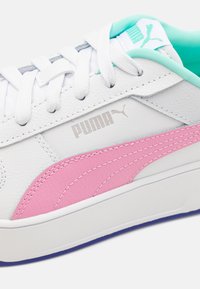 Valged tossud, millel on tekstureeritud nahk koos roosa ja tealmise aktsentidega, kinge disain ja silmatorkav hõbedane Puma logo.