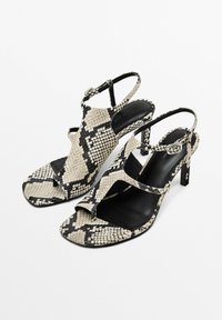 Högklackade sandaler med ormskinnsmönster i beige och svart, med öppen tå, slingback-rem och en texturerad yta på ovansidan.