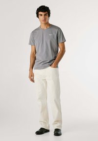 T-shirt in cotone grigio con maniche corte e piccolo logo sul petto, abbinato a pantaloni in denim bianchi e scarpe in pelle nera.