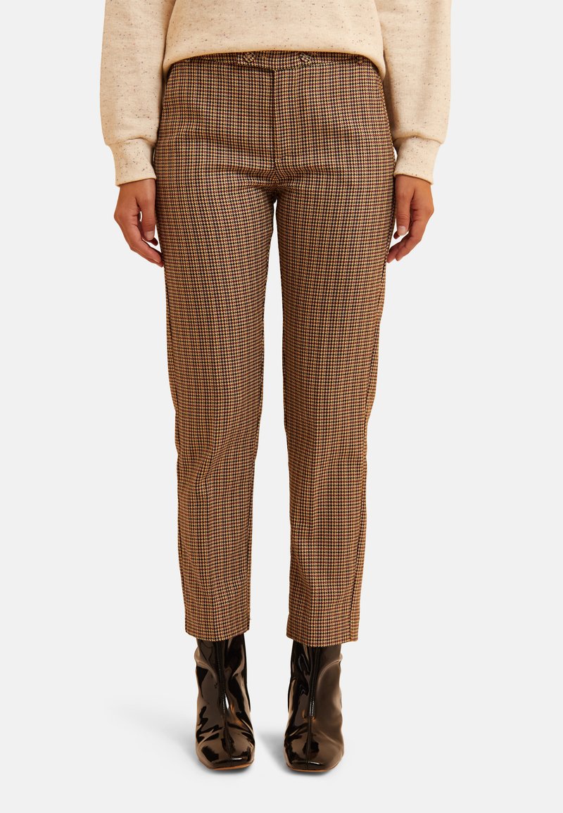 Pantalones de cuadros marrones con un ajuste ajustado, cintura alta y longitud hasta el tobillo. Combinados con botas negras de crem cierra de brillo.