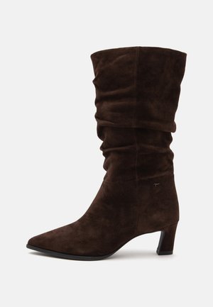 Botte mi-mollet en daim marron foncé décontractée avec bout pointu et petit talon bloc sur fond blanc.
