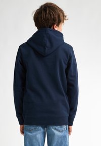Sudadera azul marino de textura suave de algodón, con bolsillo tipo canguro y capucha ajustable, combinada con jeans de mezclilla azul claro.
