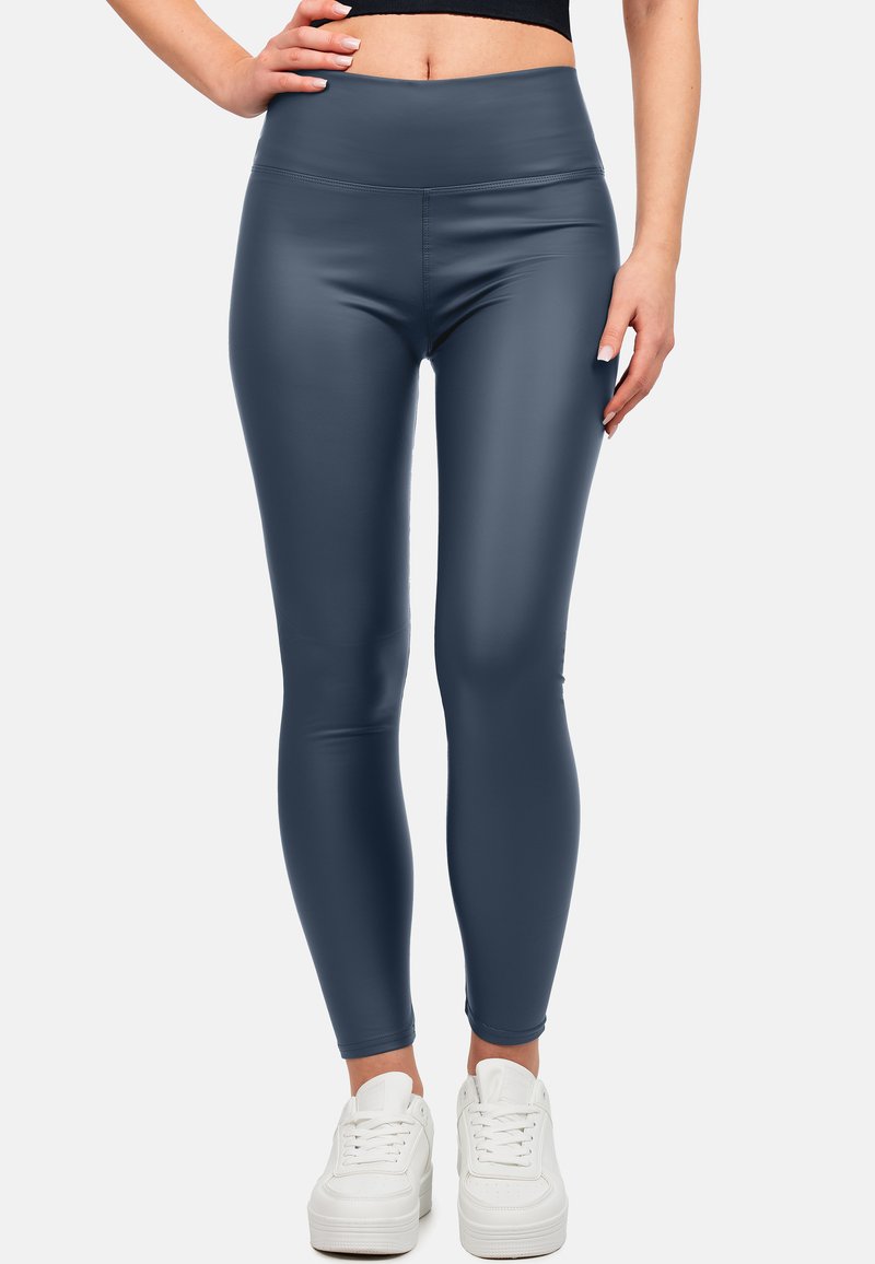 Hoog getailleerde, marineblauwe leggings gemaakt van glanzend, rekbaar materiaal. Heeft een gladde textuur en een aansluitende pasvorm, gecombineerd met witte sneakers.