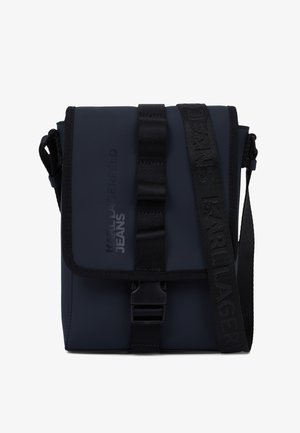 Tmavě modrá kabelka přes rameno vyrobená z hladkého, odolného materiálu, s překlopným klopou se zapínáním na pásek a s raženým logem.