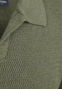 Strukturierter grüner Pullover aus Strickstoff mit einem gerippten Muster und umgeschlagenem Kragen. Das Material wirkt weich und flexibel.