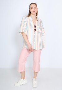Blouse à manches courtes rayée dans des couleurs pastel, avec une poche poitrine, accompagnée de pantalons rose crop et de baskets blanches.