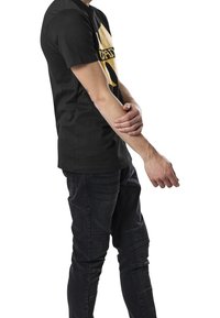 Zwarte katoenen t-shirt met een gele grafische print aan de voorkant. Draagt bij donkere spijkerbroek met textuuraccenten en stiksels.