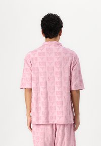Short-sleeved pink shirt with textured fabric, featuring a pattern of square designs and symbols. Collar and casual fit.