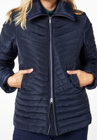 Námorně modrá péřová bunda s předním zipem, stojáčkem a diagonálně prošívaným vzorem. Obsahuje boční kapsy a hladkou texturu.