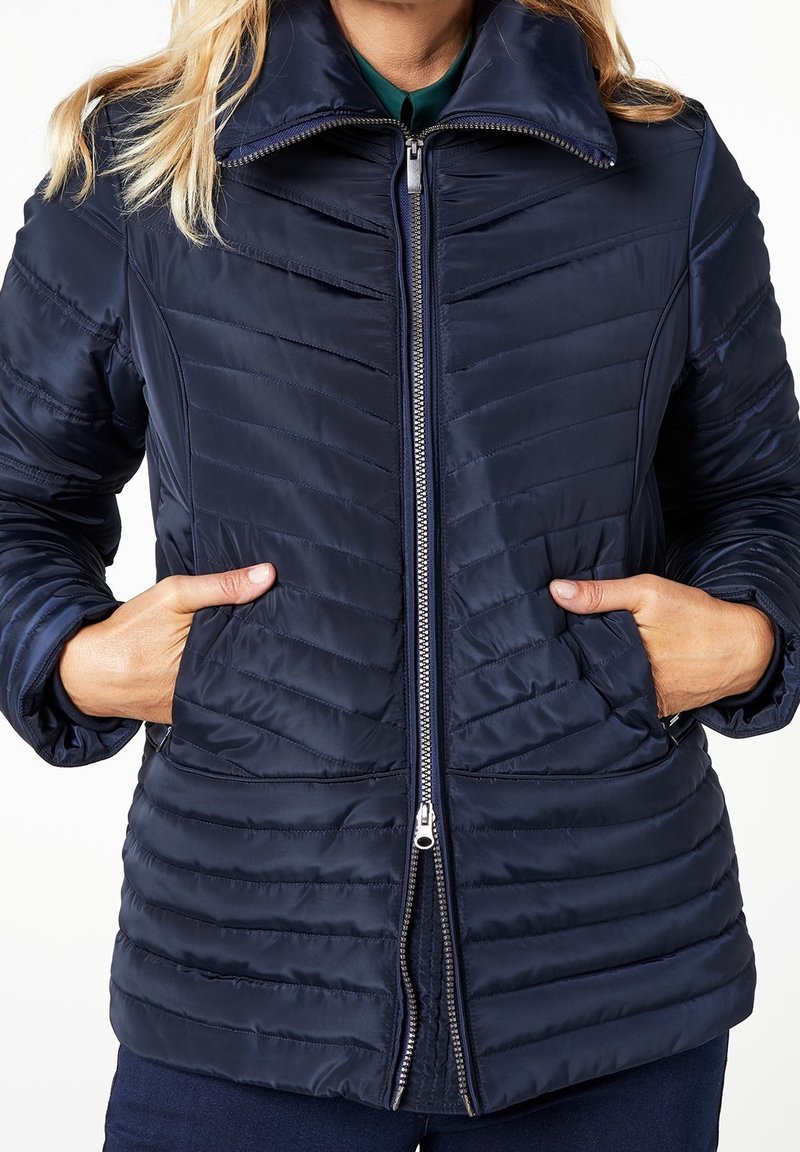 Námorně modrá péřová bunda s předním zipem, stojáčkem a diagonálně prošívaným vzorem. Obsahuje boční kapsy a hladkou texturu.