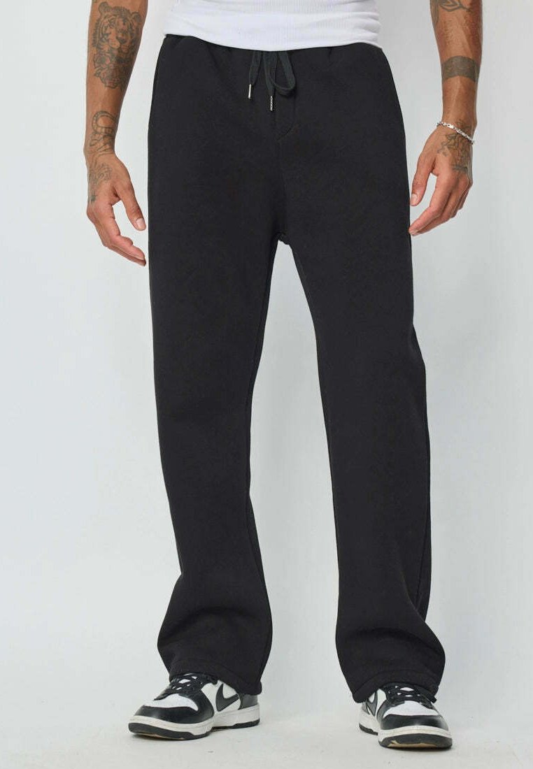 Pantalons de survêtement noirs avec une taille à cordon, coupe décontractée et poches latérales, fabriqués en tissu doux et texturé. Associés à des baskets.